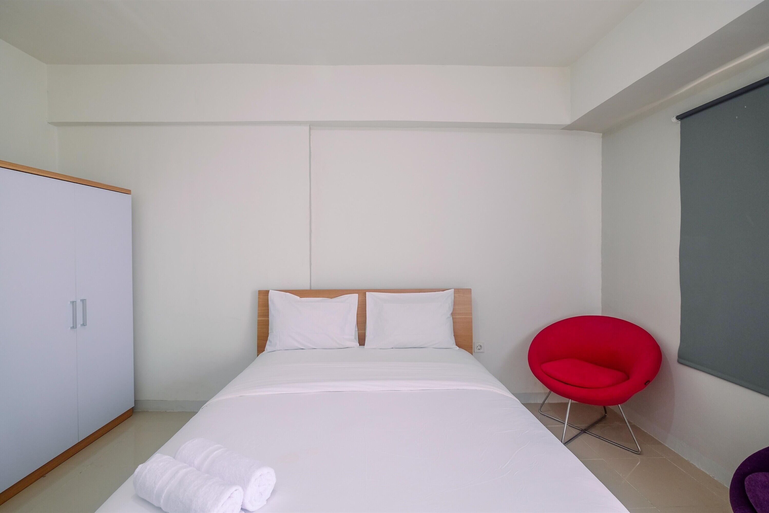A bedroom with a bed, a wardrobe, a red chair, and a window.