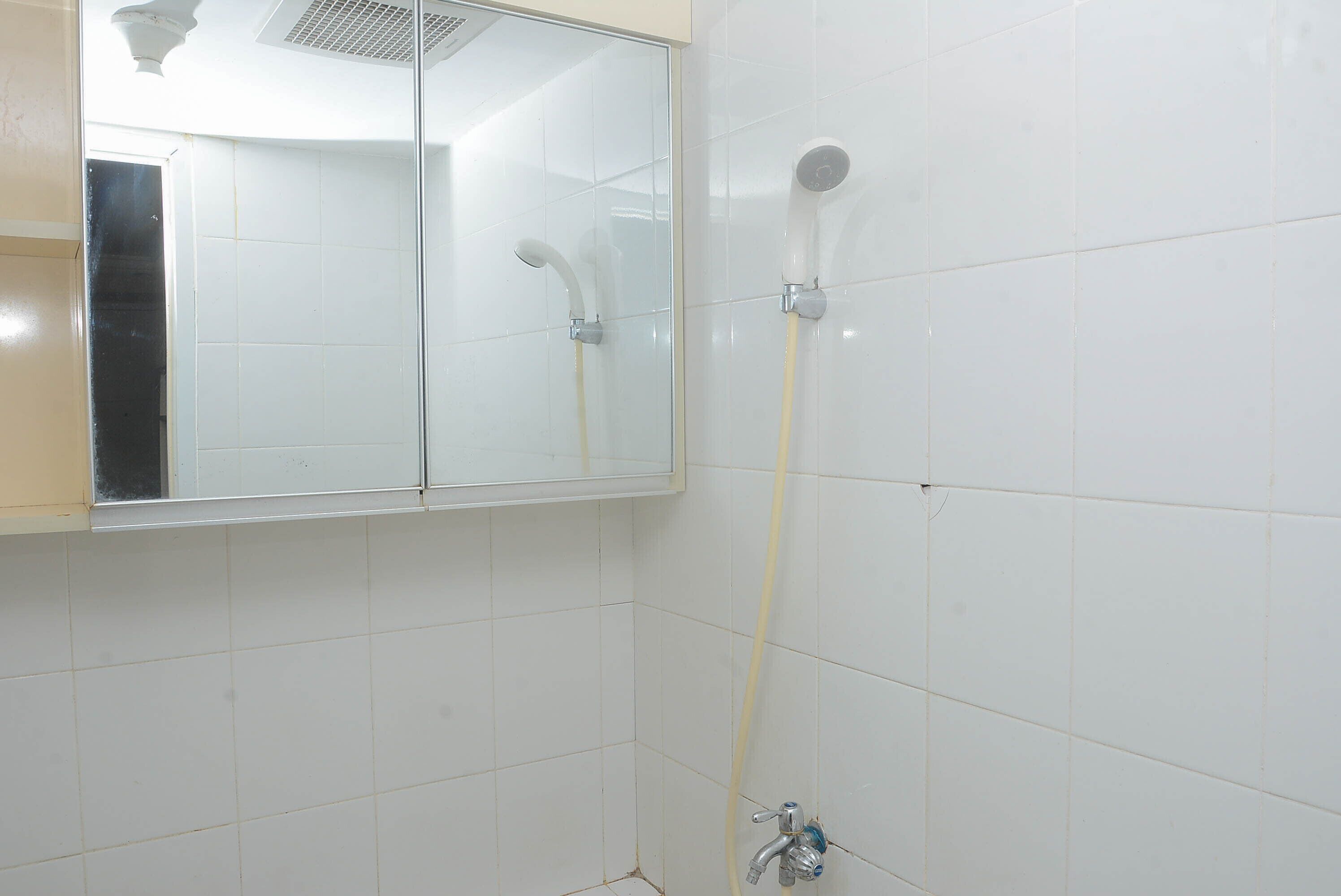 A bathroom with white tiles, a mirror, and a shower with a handheld showerhead and a wall-mounted showerhead.