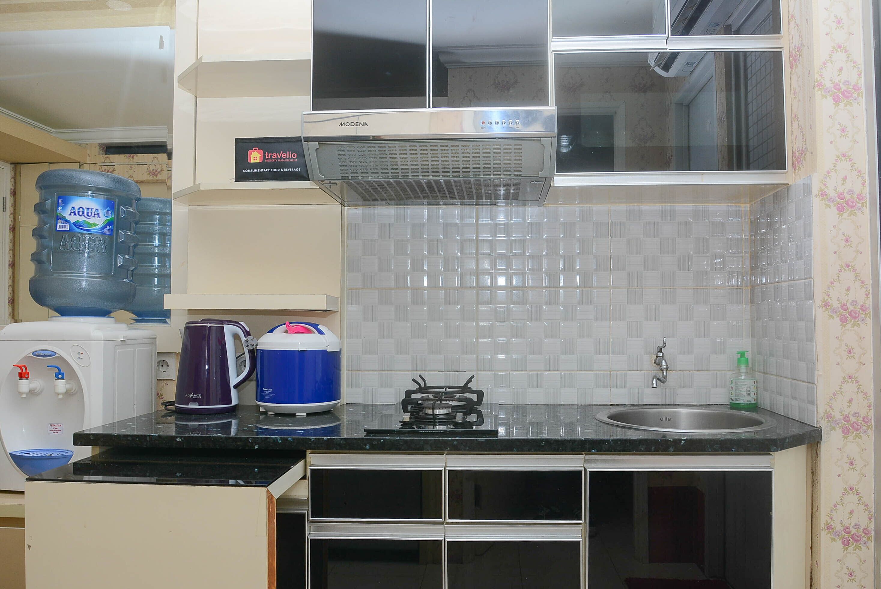 A compact kitchen with a water dispenser, a kettle, a stove, and a sink.