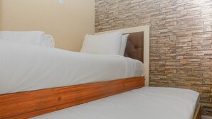 A bed with a wooden headboard and white bedding in a room with a stone-patterned wall.