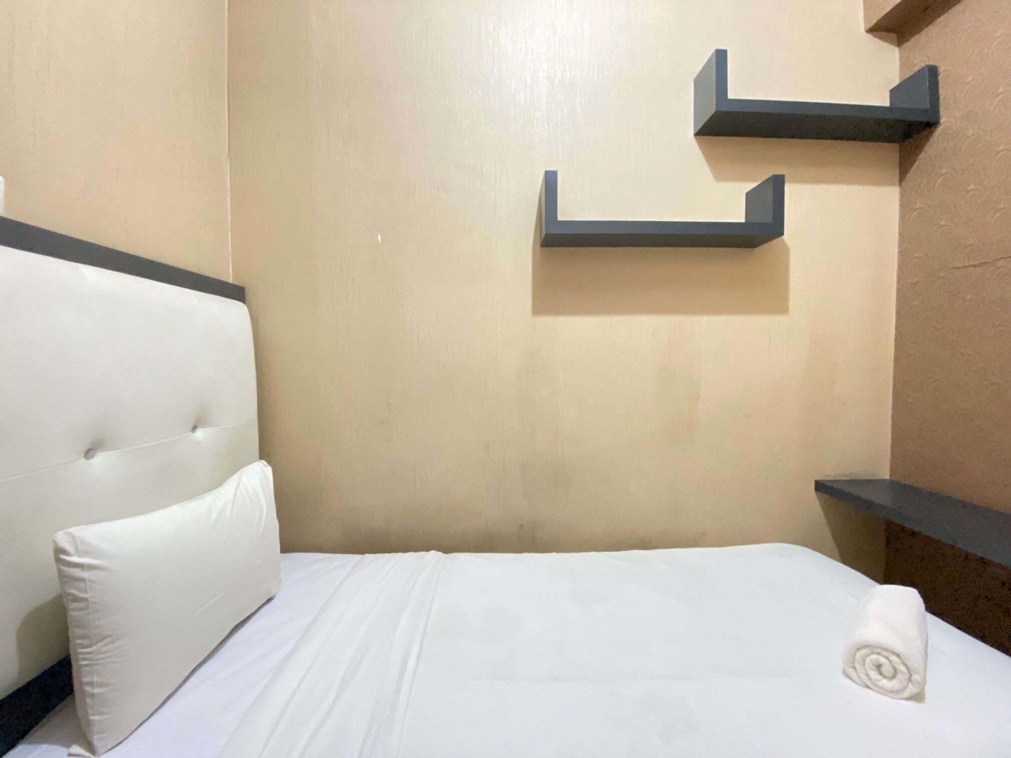 Ein Hotelzimmer mit einem weißen Bett, einem gepolsterten Kopfteil und zwei dunklen Wandschränken.