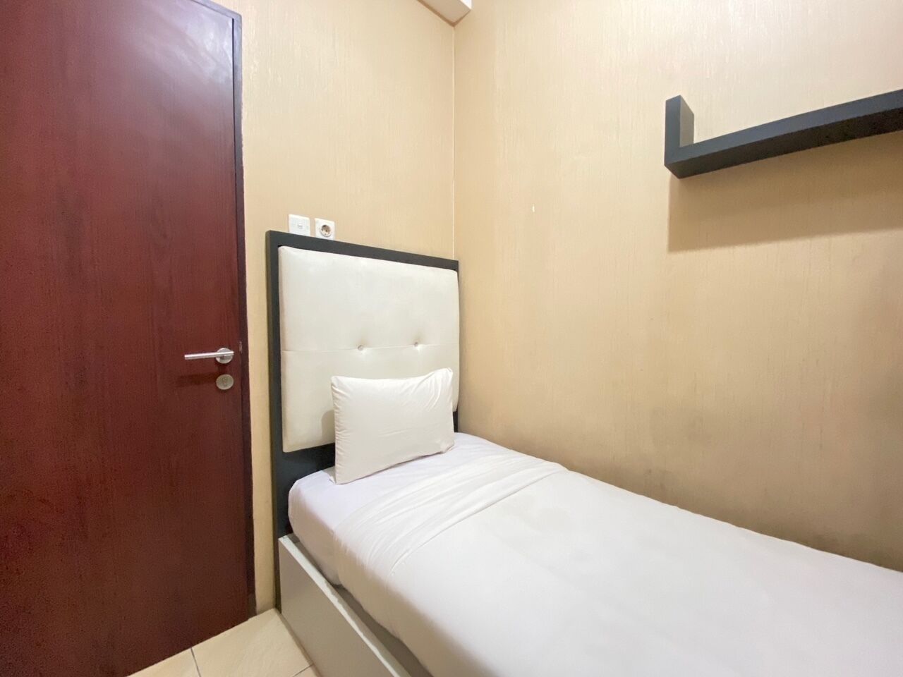 Una habitación pequeña con cama individual, puerta de madera, cabecera y colchón blancos.