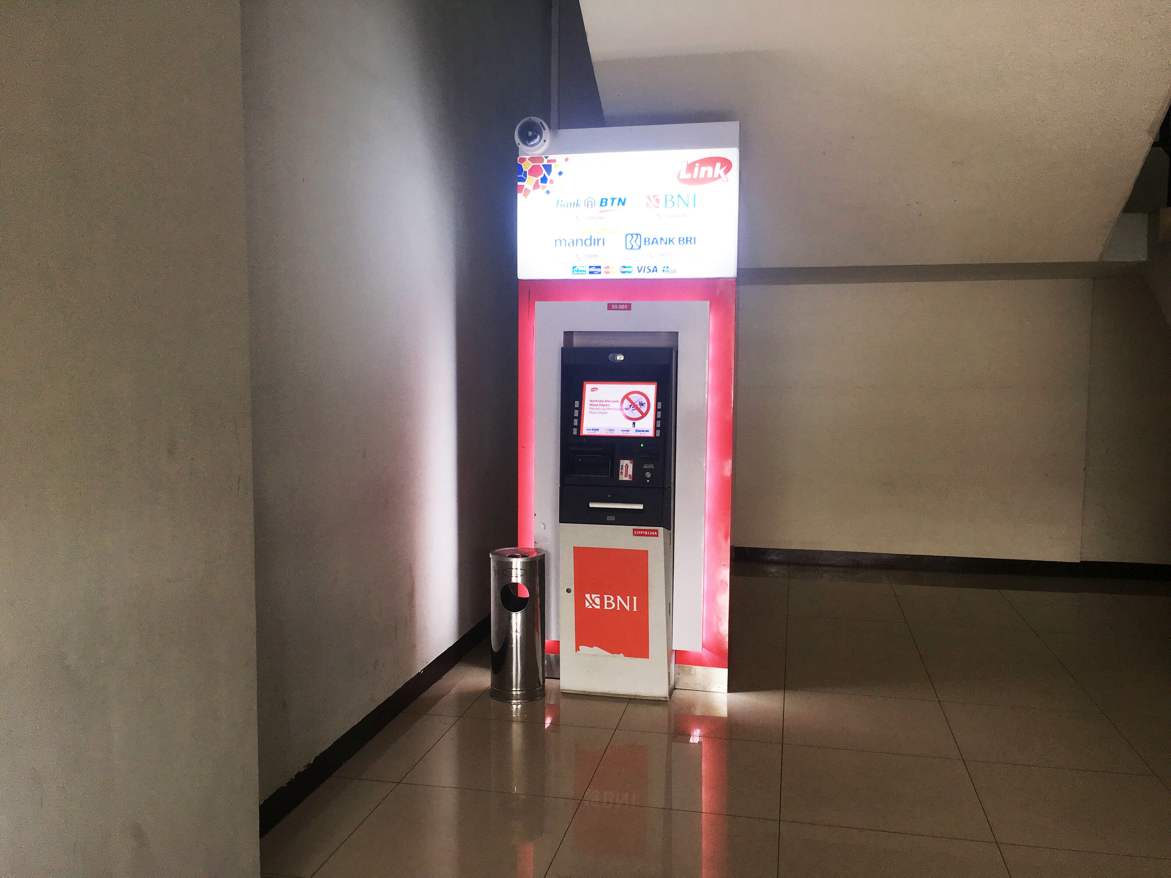 A self-service ATM kiosk with a digital screen, a trash can, and a red sign with BNI branding.