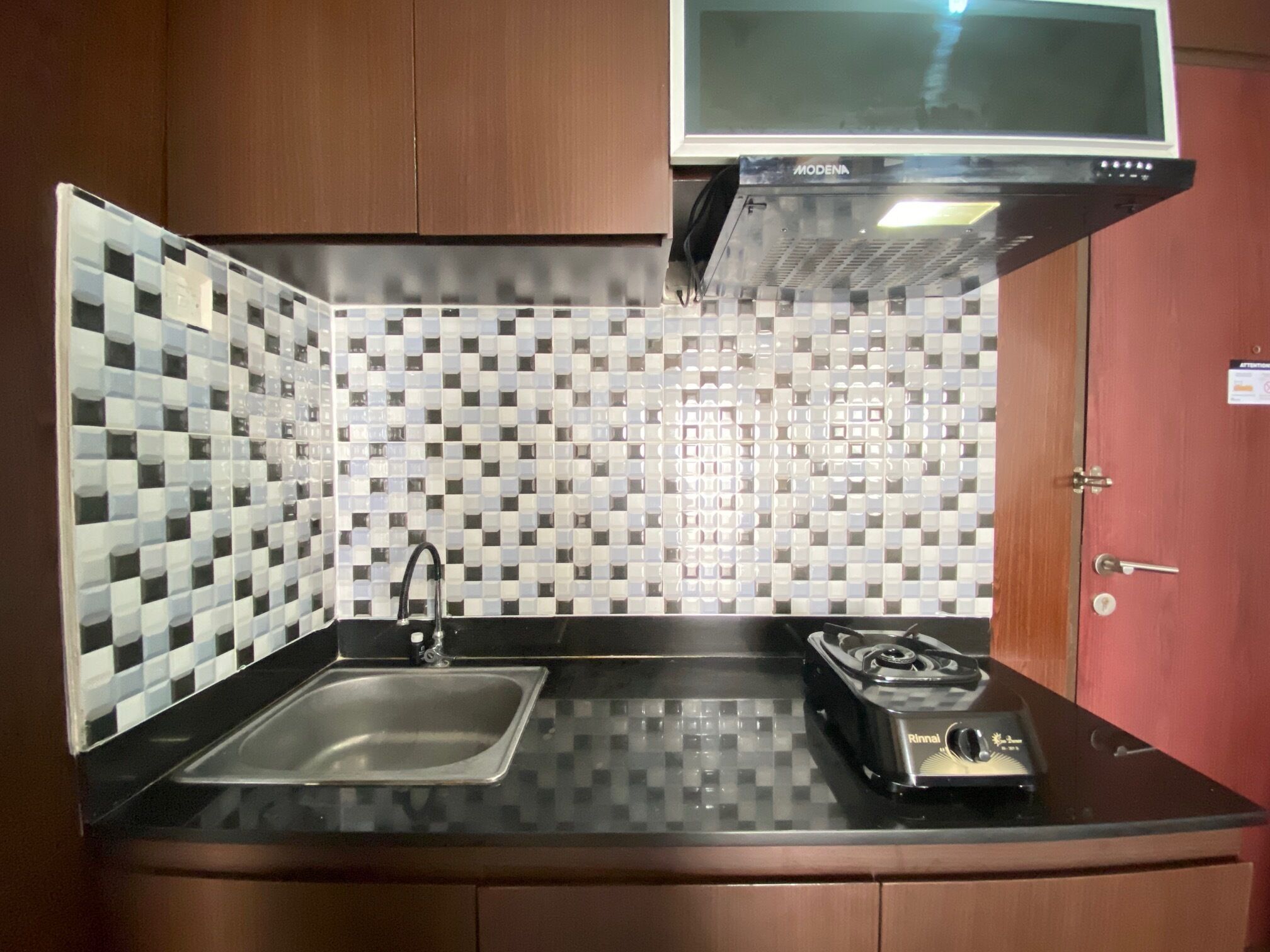 Cocina compacta con salpicadero a cuadros, un lavamanos de acero inoxidable, una estufa a gas y un microondas sobre la estufa.
