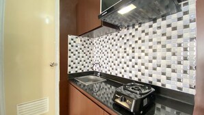 A compact kitchen with a black countertop, a sink, a stove, and a backsplash with a checkered tile pattern. - Spacious 1BR at Tamansari Panoramic Apartment near Metro Indah Mall (Bandung)