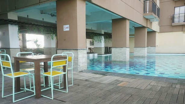 An indoor swimming pool with a wooden table and chairs, surrounded by beige pillars and a tiled floor. - Spacious 1BR at Tamansari Panoramic Apartment near Metro Indah Mall (Bandung)