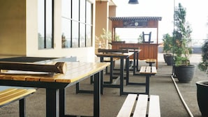An outdoor seating area with wooden tables and benches, potted plants, and a view of the street. - Spacious 1BR at Tamansari Panoramic Apartment near Metro Indah Mall (Bandung)