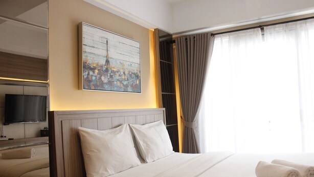A hotel room with a bed, a flat-screen TV, a painting, and a window with curtains. - Luxurious Studio Room @ Grand Asia Afrika Apartment (Bandung)