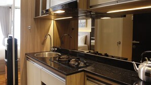 A compact kitchen with a stainless steel sink, a gas stove, and a kettle. - Luxurious Studio Room @ Grand Asia Afrika Apartment (Bandung)