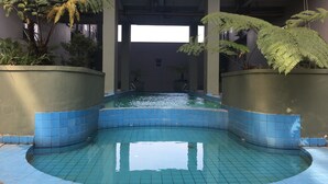 A swimming pool with blue tiles, surrounded by planters with ferns and other greenery. - Luxurious Studio Room @ Grand Asia Afrika Apartment (Bandung)