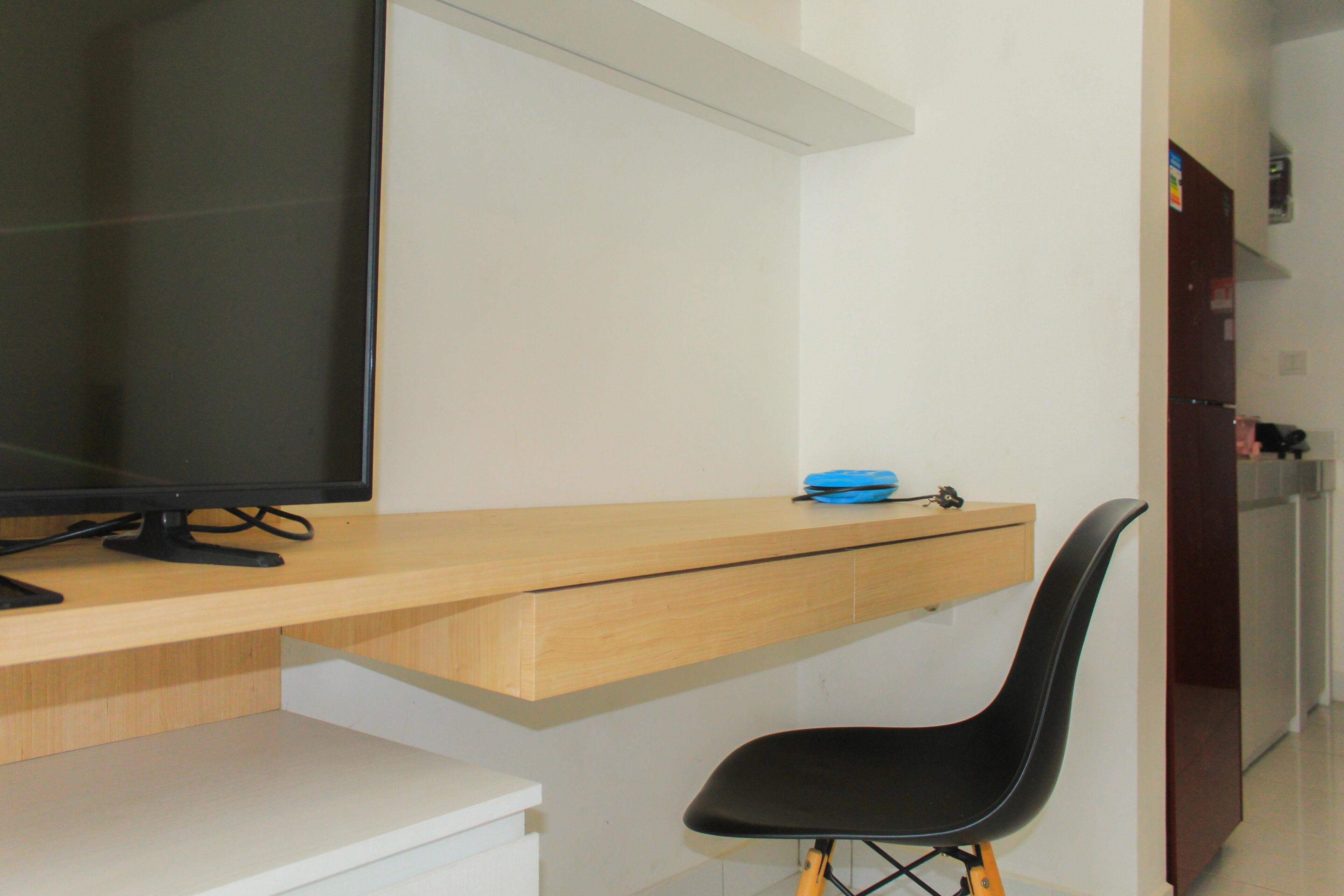 Una habitación moderna con un escritorio de madera, una silla negra y un televisor.