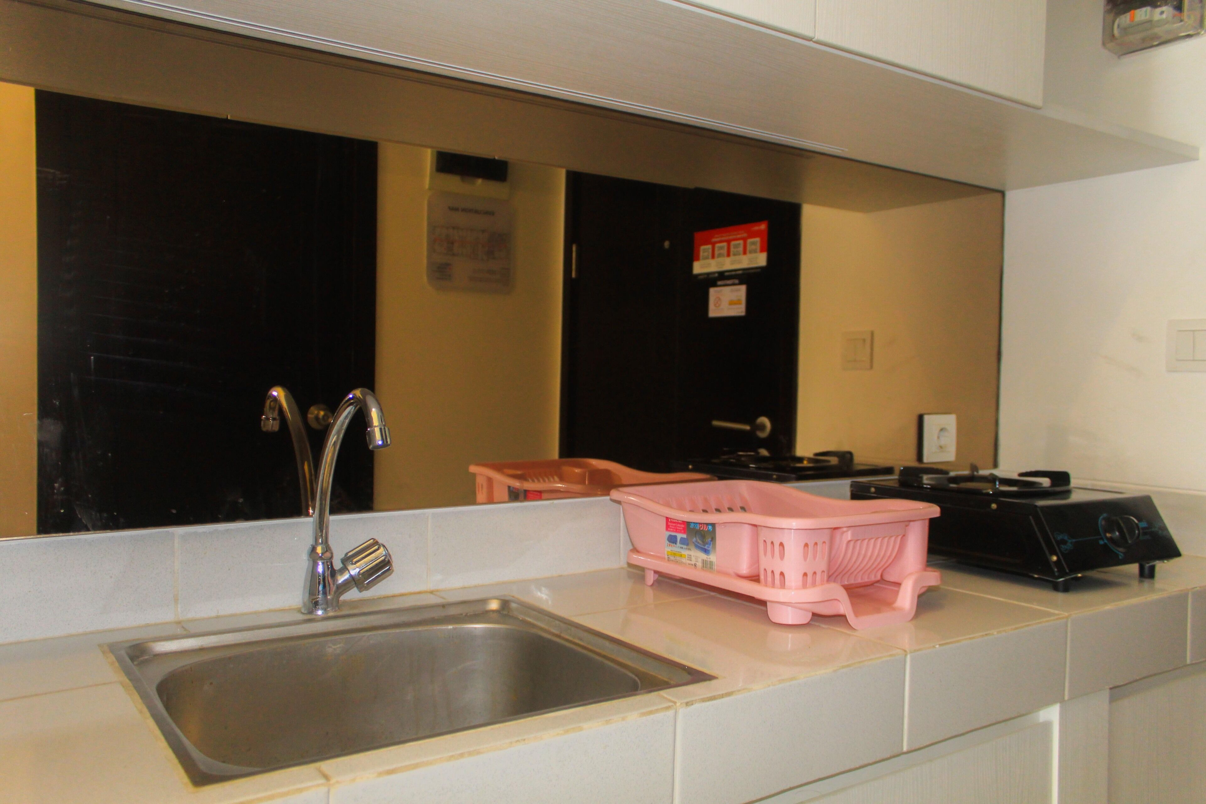 Et køkken med en stålvask, en pink plastik kurv og en sort komfur.