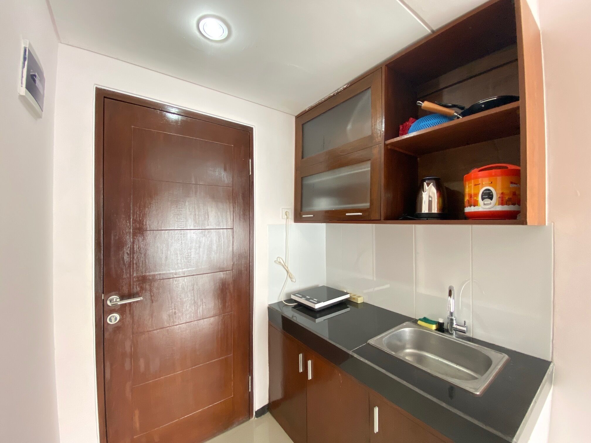 A compact kitchen with a wooden door, a stainless steel sink, and a microwave on the countertop.