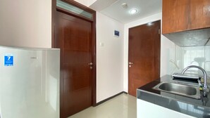 A kitchen with a refrigerator, two wooden doors, a sink, and a ceiling light.