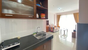 A modern kitchen with a black countertop, stainless steel sink, and wooden cabinets. There is a dining area with a sofa and a table in the background.