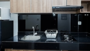 A modern kitchen with a black countertop, stainless steel sink, and a gas stove. - Stylish and Comfy Studio at Casa De Parco Apartment (Pagedangan)