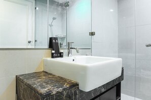 A modern bathroom with a white sink, a marble countertop, and a glass shower enclosure.