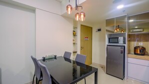Una cocina moderna con una mesa de comedor de vidrio, dos sillas, un microondas integrado, un refrigerador de acero inoxidable y una lámpara colgante.