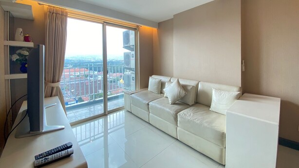 A modern living room with a white sofa, a flat-screen TV, and a large window offering a city view.