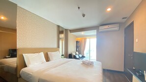 A hotel room with a large bed, a flat-screen TV, a desk, and a window with curtains.