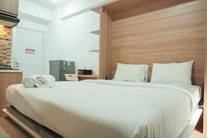 A hotel room with a large bed, a wooden headboard, a small desk with a chair, and a bathroom sign.