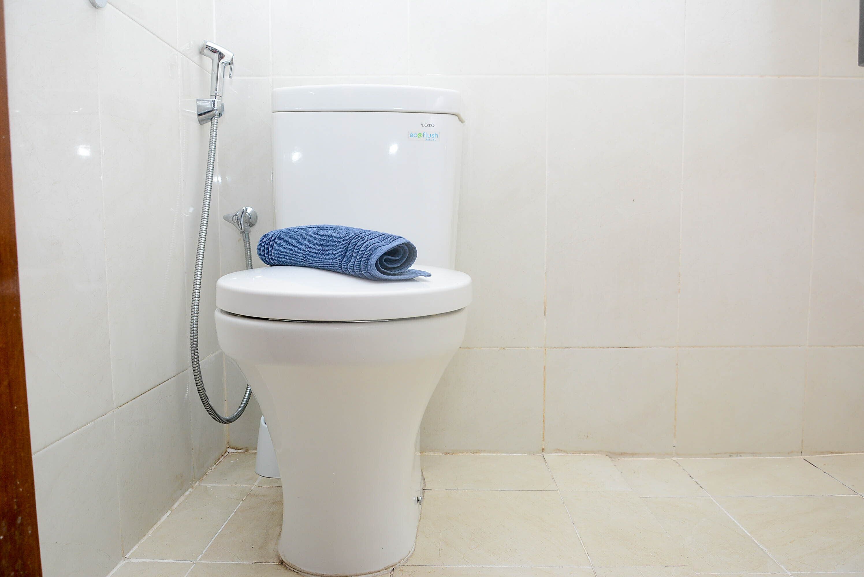 A white toilet with a blue towel on top, a shower hose, and a Toto ecologic flush toilet.