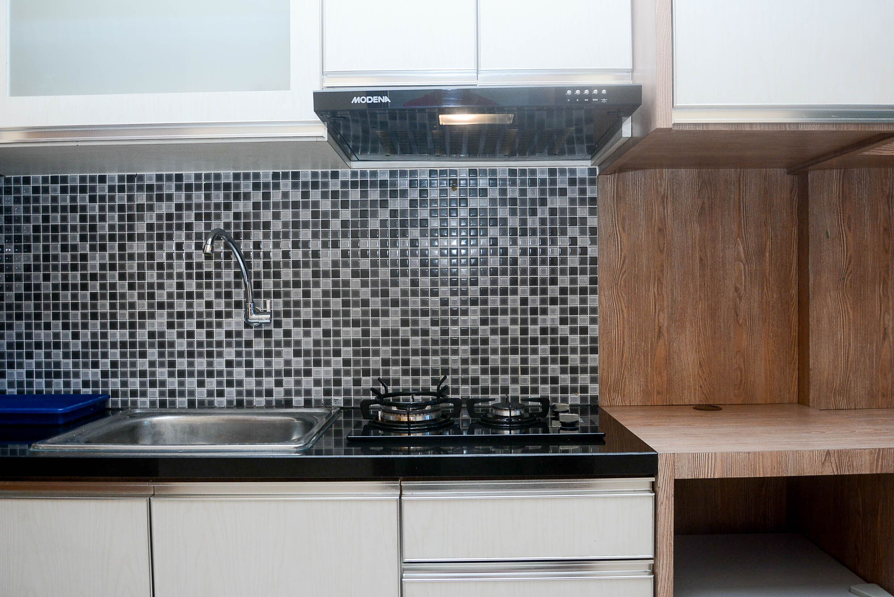 A kitchen with a black countertop, a stainless steel sink, a gas stove, and a backsplash made of small, square tiles in a dark color.