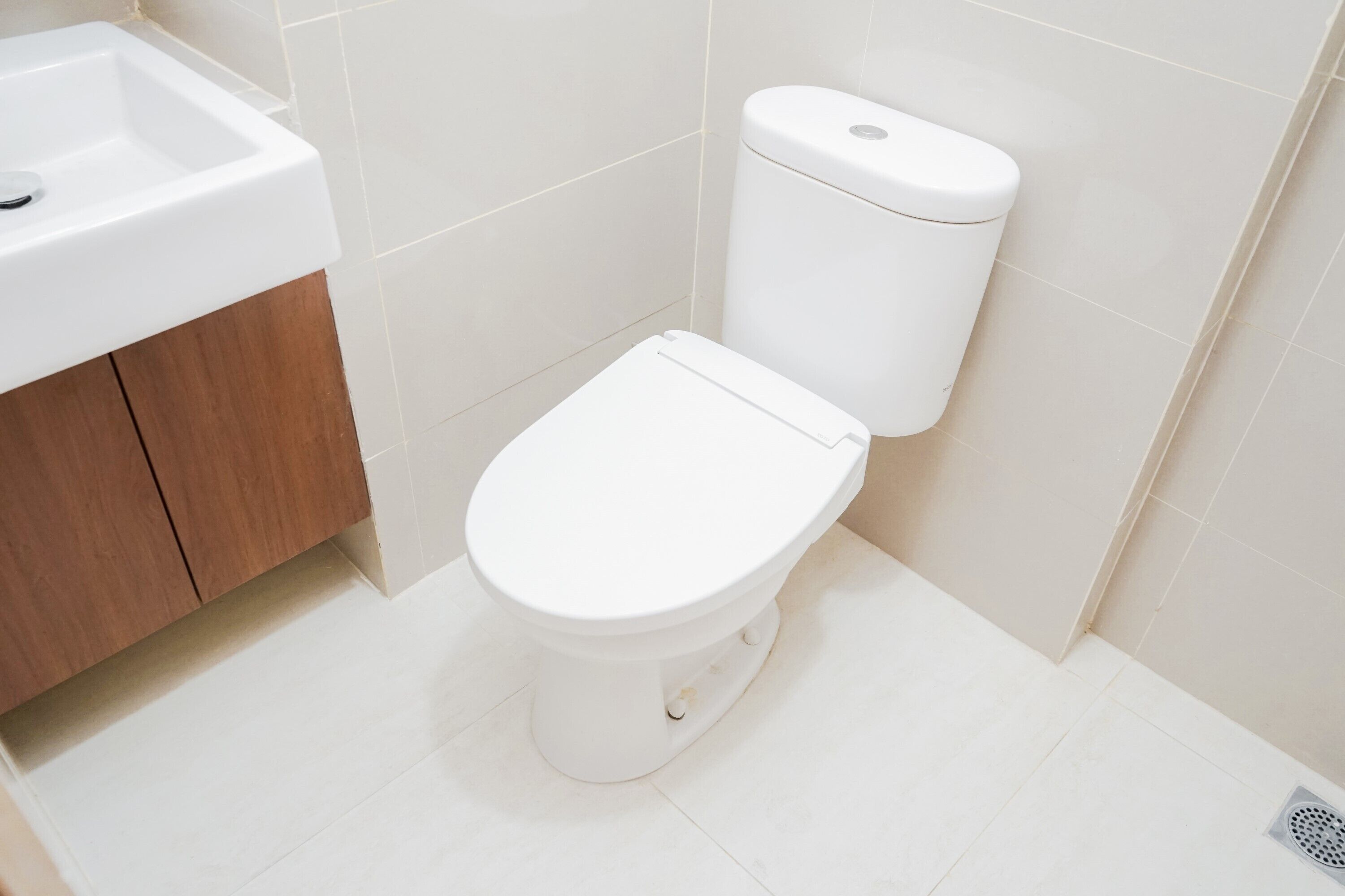A small, clean bathroom with a white toilet, a wooden cabinet, and a white sink.