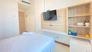 A hotel room with a bed, a mounted TV, a mini-fridge, and a shelf with toiletries.