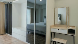 Une chambre d’hôtel moderne dotée d’une grande porte coulissante donnant sur un balcon, d’un lit avec une tête de lit en bois, d’une table de chevet avec un miroir et d’un petit bureau avec une chaise.