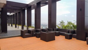 Une terrasse sur le toit, agrémentée de colonnes sombres, de meubles en osier et offrant une vue sur le paysage urbain.