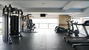 Une salle de sport moderne dotée de divers équipements d’exercice, notamment des tapis de course et des appareils de musculation, et de grandes fenêtres offrant une vue sur la ville.