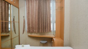 A bedroom with a bed, a mirror, a window with curtains, a stool, and a towel on the bed. - Relaxing 2BR at Menteng Square Apartment (Jakarta)