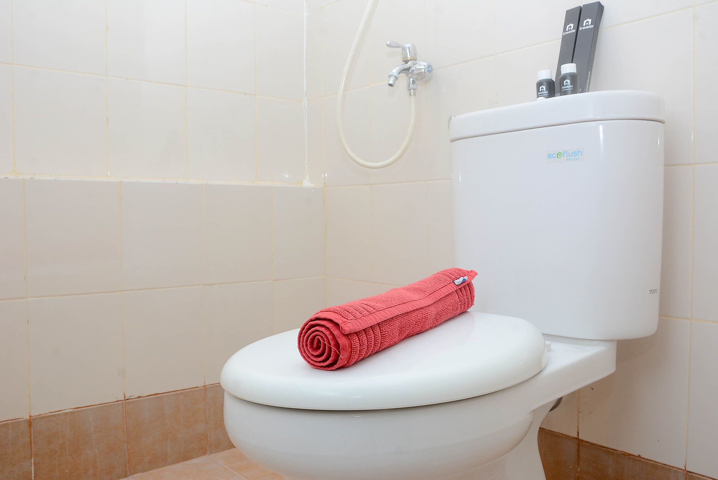 A white toilet with a red towel on the seat and a shower head above it.