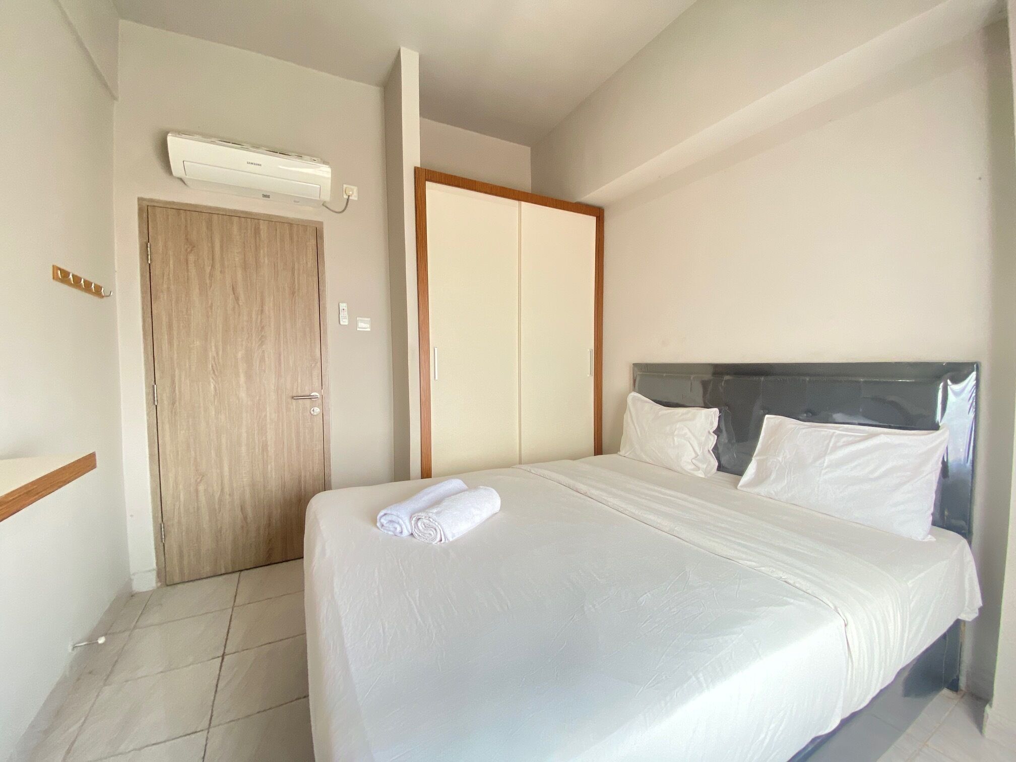 A hotel room with a bed, a wooden door, a wardrobe, and an air conditioning unit.