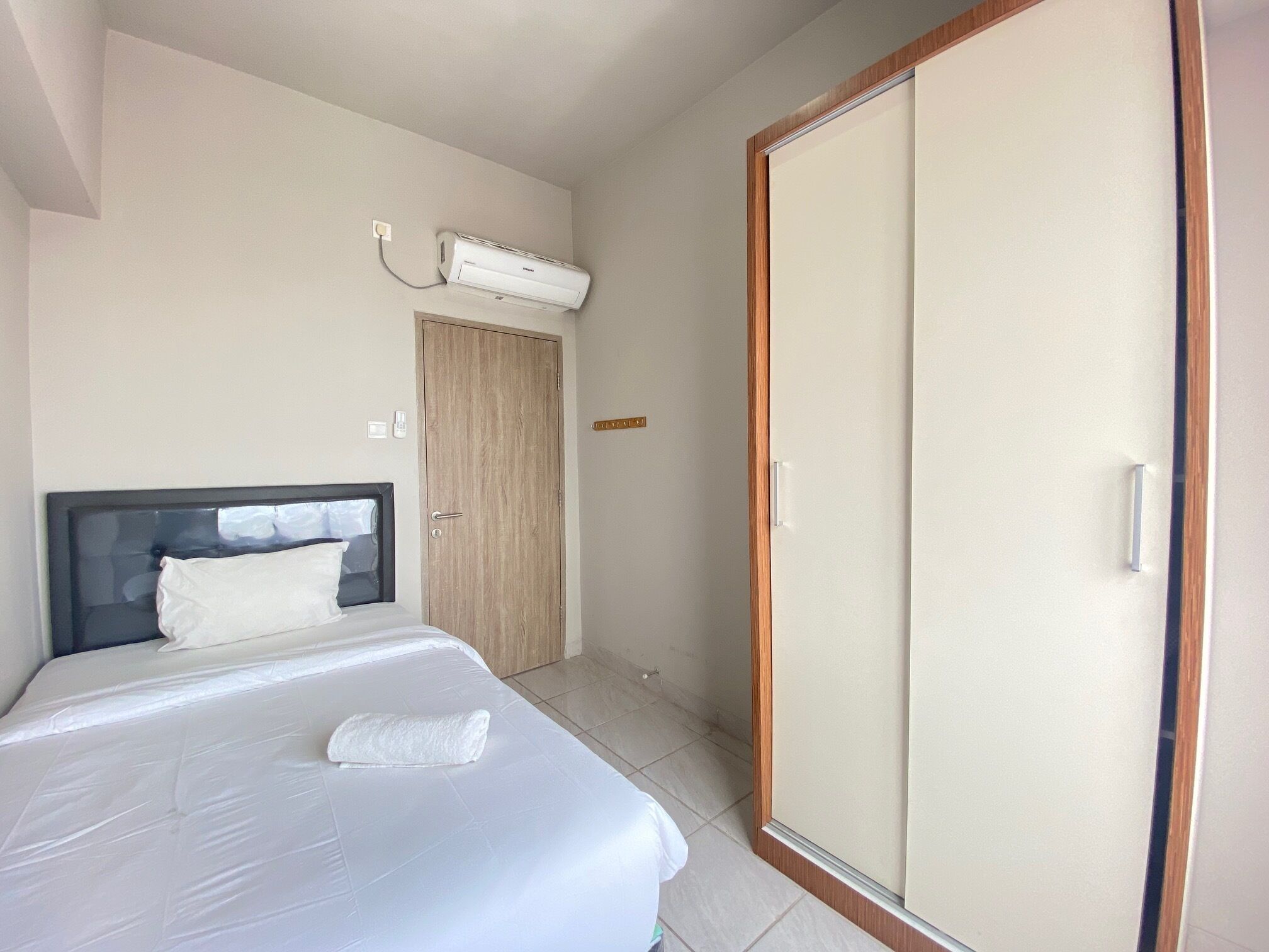 A hotel room with a bed, an air conditioning unit, a wardrobe, and a door.