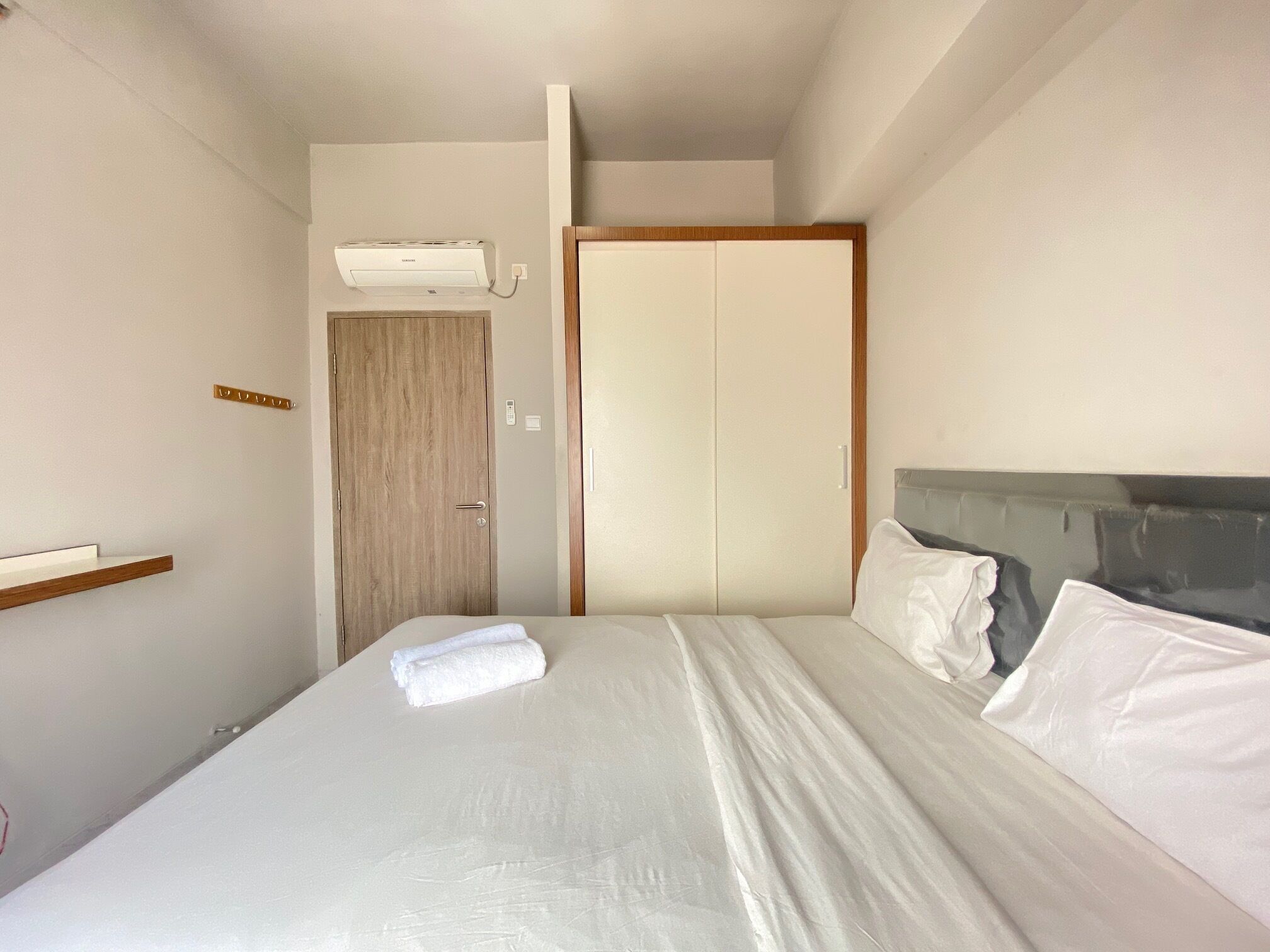 A hotel room with a bed, a wooden wardrobe, and a wall-mounted air conditioner.