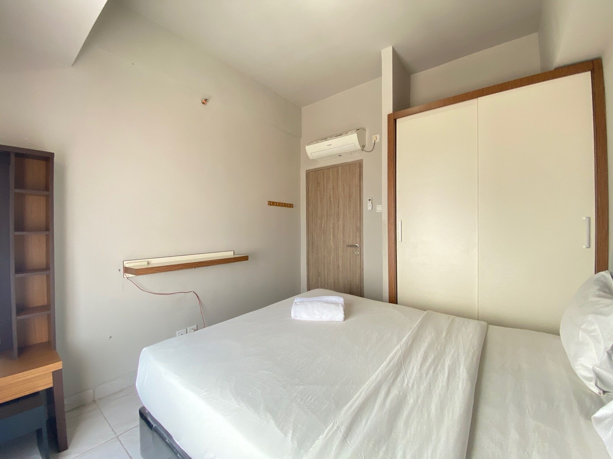 A bedroom with a bed, a wooden shelf, a wardrobe, and an air conditioning unit.