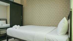 A neatly made bed with white linens and pillows, a dark metal frame, and a textured beige wall behind it.