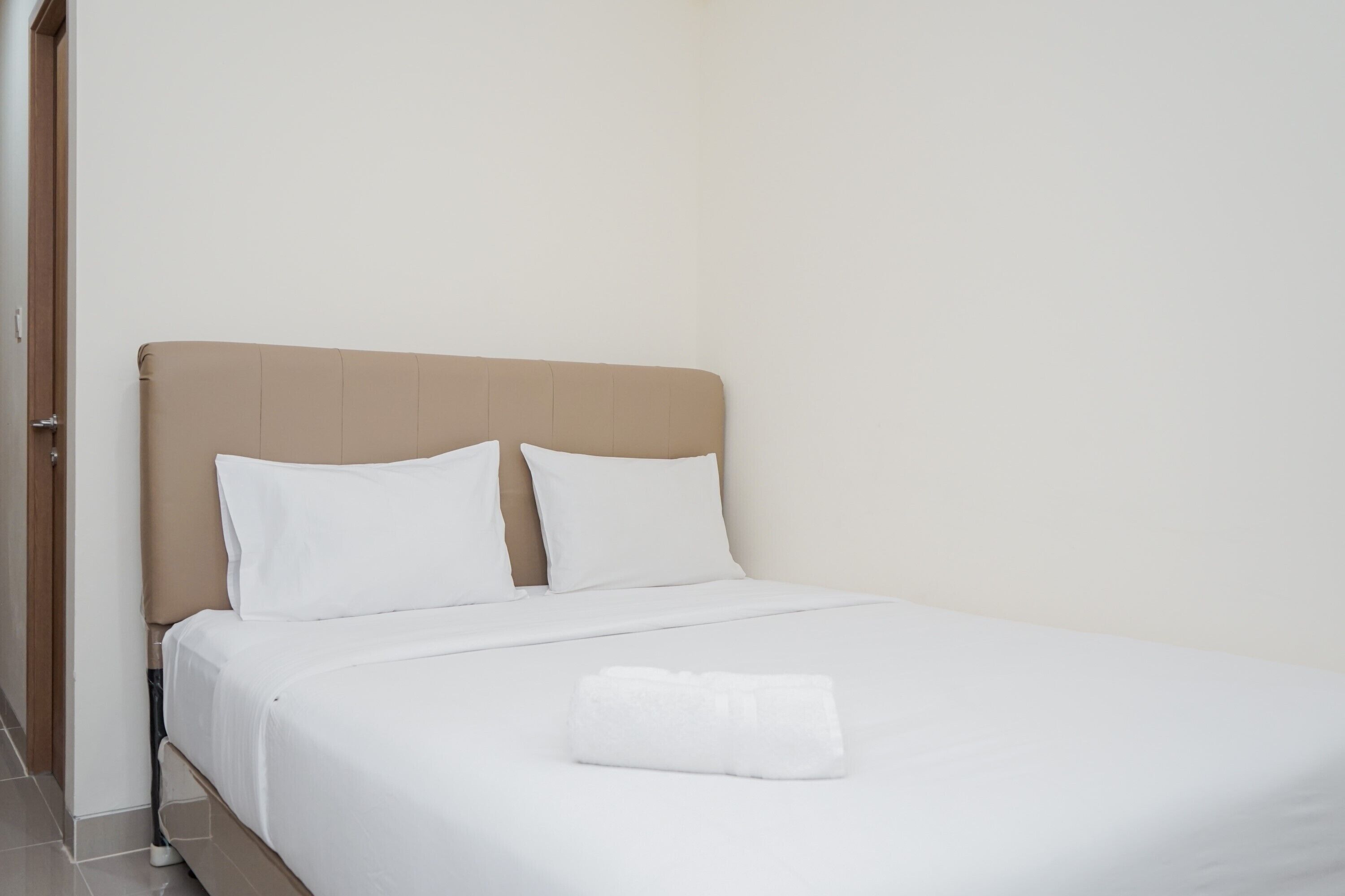 Una cama bien hecha con sábanas blancas y una toalla blanca doblada encima.