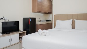 A hotel room with a bed, a television, a minibar, and a kitchenette. - Comfy Studio Apartment at B Residence (Pagedangan)