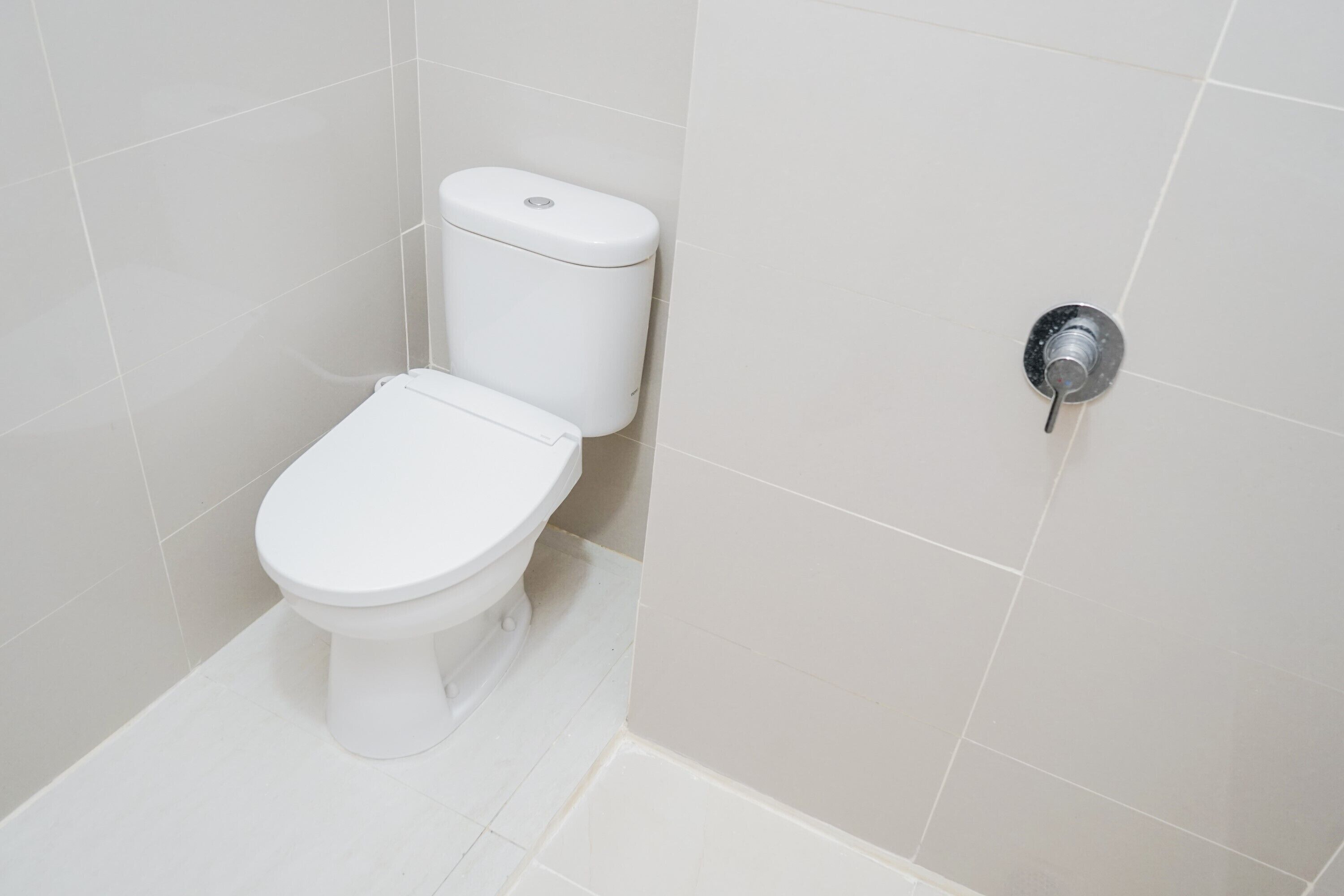 A white toilet in a corner of a bathroom with white tiles.