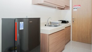 A kitchen with a black refrigerator, a sink, wooden cabinets, and a door with a sign. - Comfy Studio Apartment at B Residence (Pagedangan)