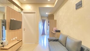 Una habitación de hotel moderna con un armario de madera, un televisor de pantalla plana, un sofá y una mesita con un ventilador.