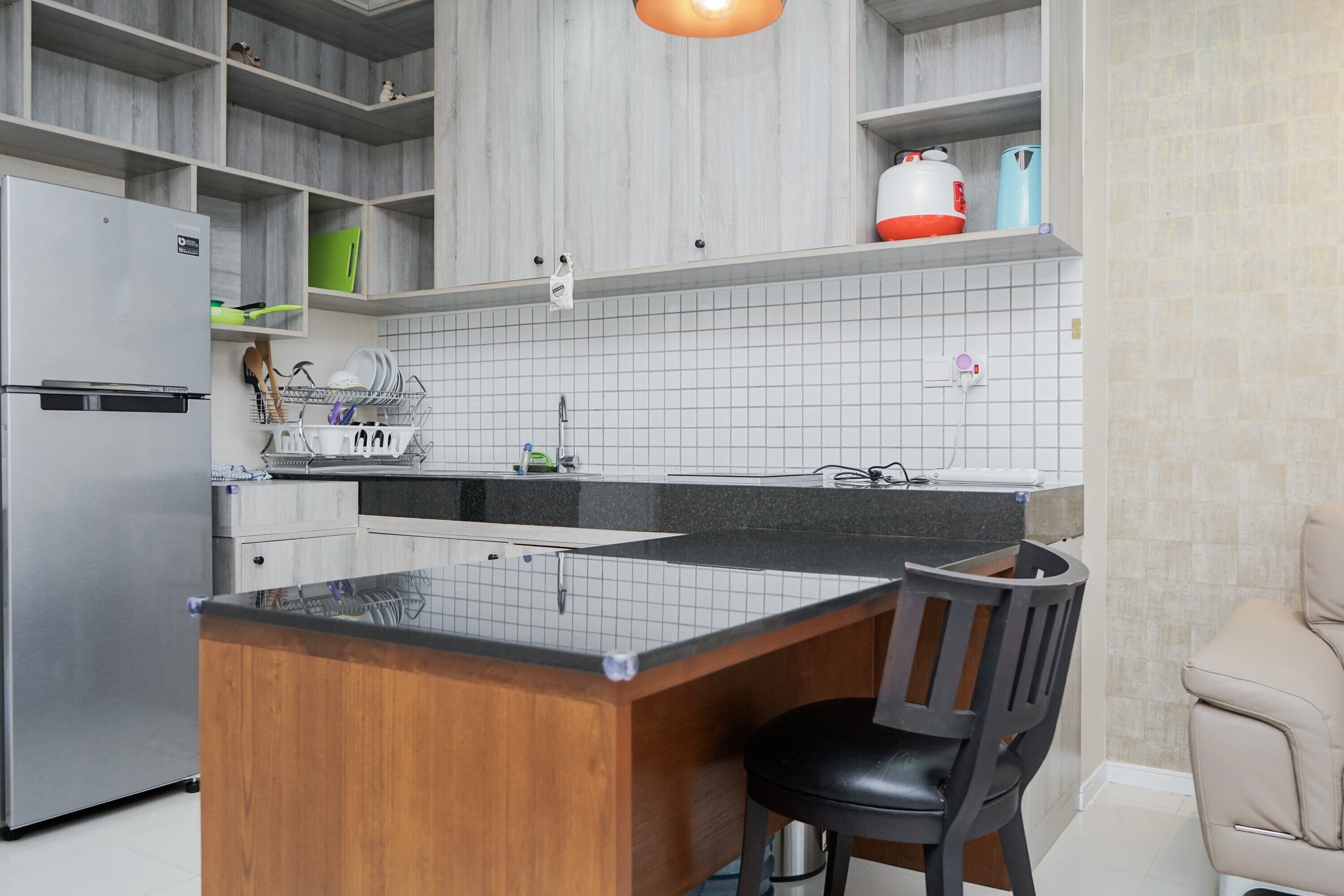 Une cuisine moderne dotée d’un îlot central, d’un réfrigérateur encastré et d’un coin salon avec une chaise.