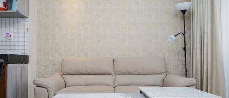 En stue med en beige sofa, et marmorbord, en gulvlampe og en flisevæg med et klimaanlæg.