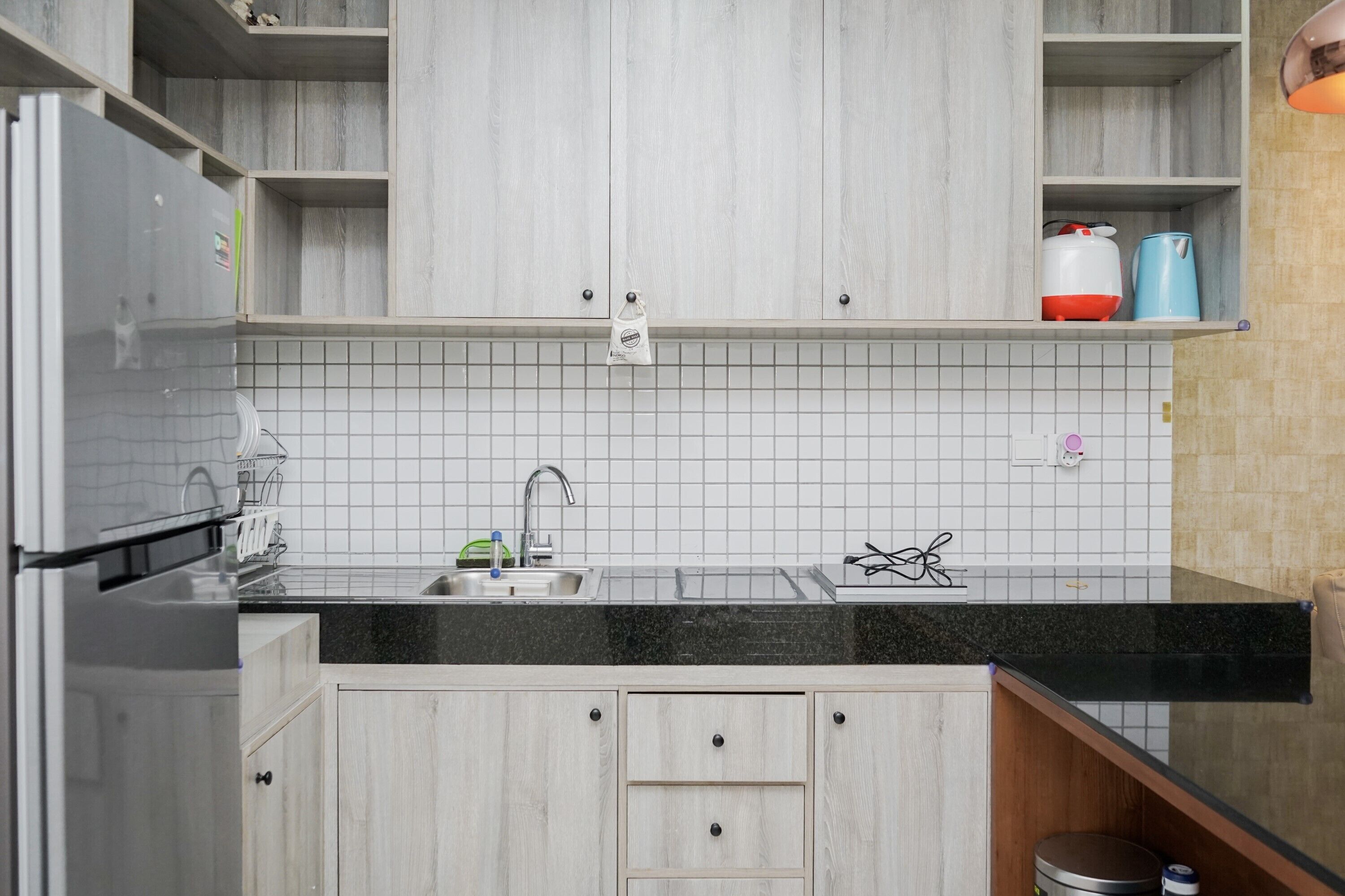 Una cocina moderna con armarios blancos, encimera negra y refrigerador de acero inoxidable.
