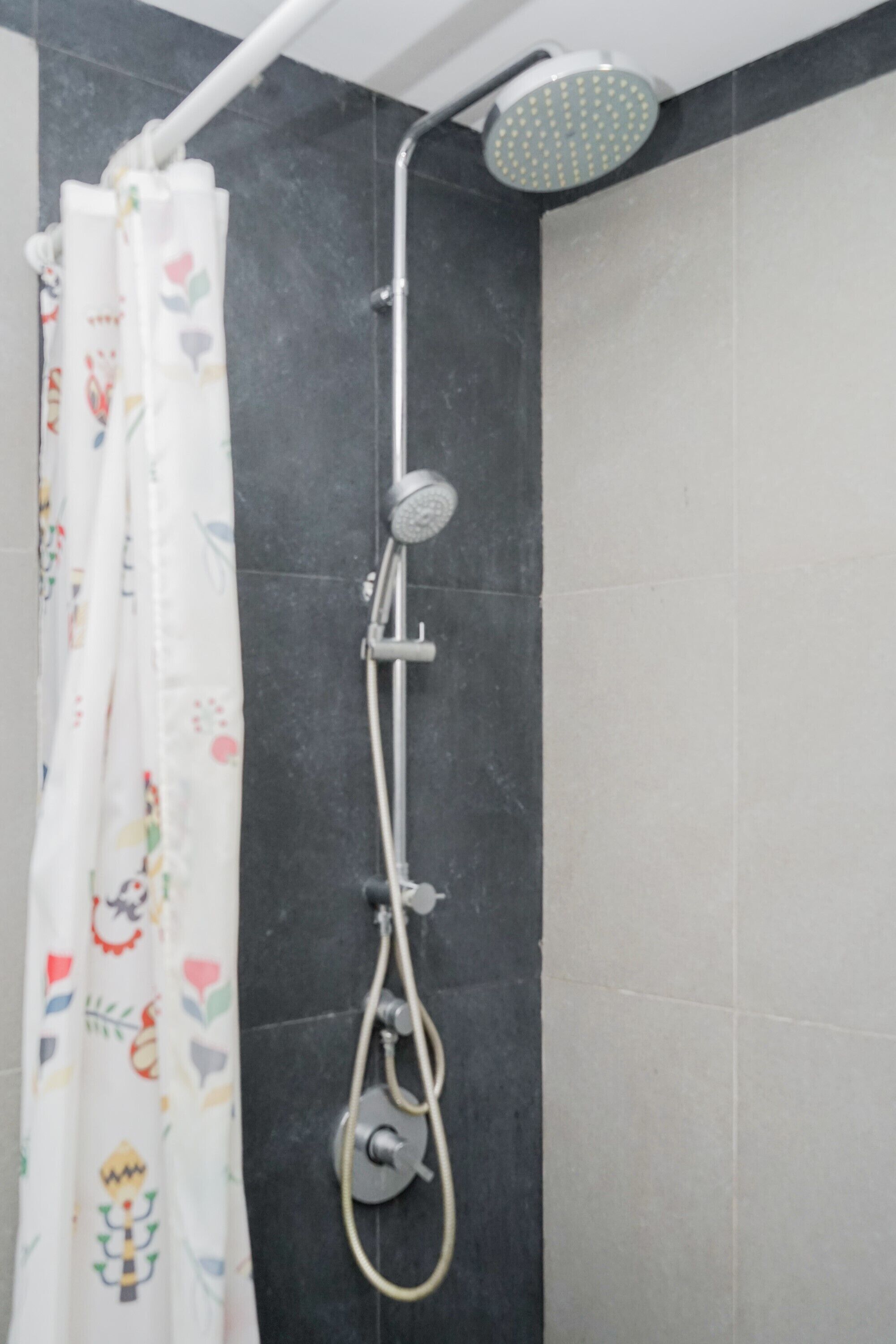 Un área de ducha con cabezal de ducha, un cabezal de ducha de mano y una cortina con un diseño colorido.