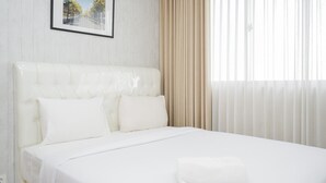A neatly made bed with white linens and pillows, a framed picture on the wall, and sheer curtains on the window.