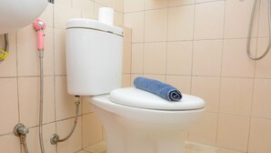 A white toilet with a blue towel on the seat, a pink handheld showerhead, and a metal drain cover on the floor. - Homey Studio Pakubuwono Terrace Apartment (Jakarta)